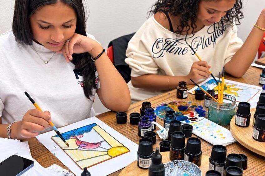 Two people painting at a table with various art supplies. 3