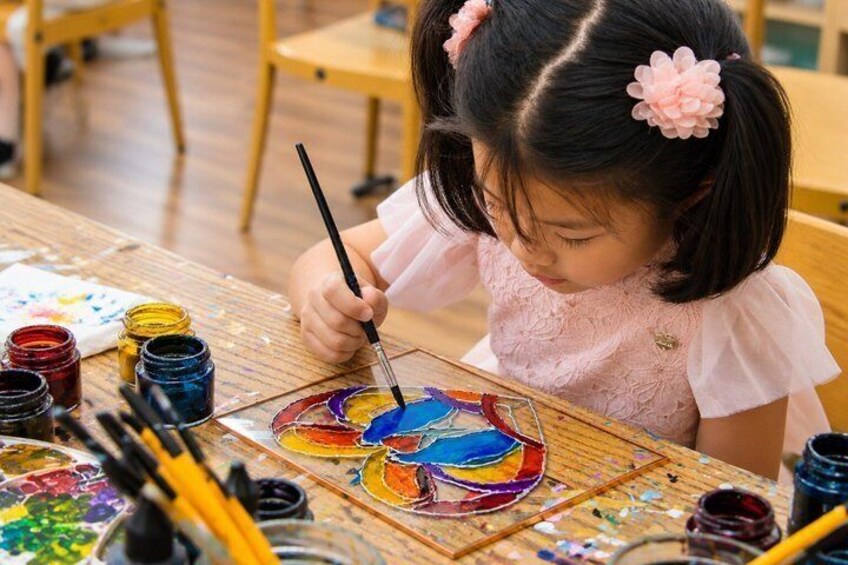 A child painting on a canvas with various colors of paint around. 1