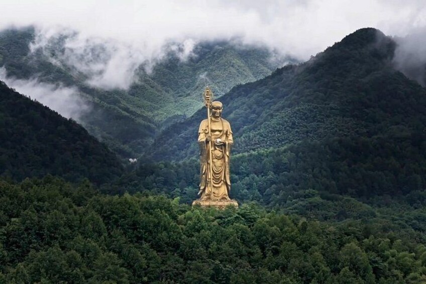 A large golden statue in a forested valley with mountains in the background. 1