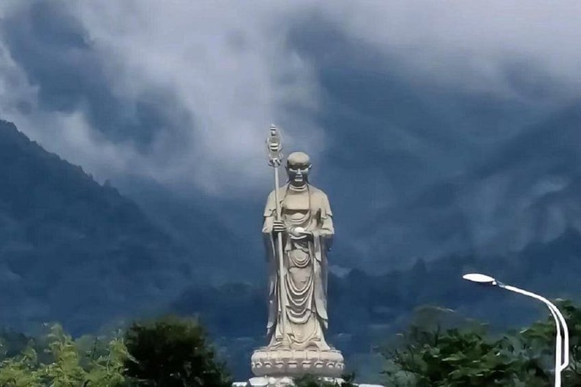 A statue of a figure holding a staff, set against a backdrop of mountains and cloudy sky. 2