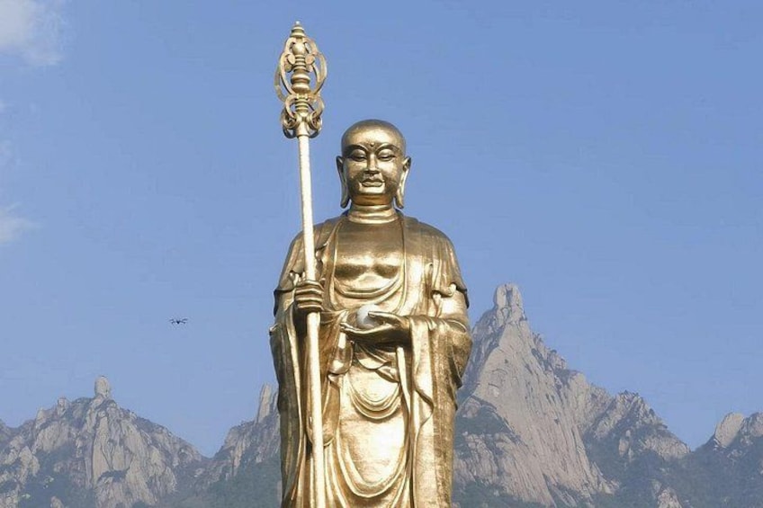 A golden statue of a figure holding a staff, set against a mountainous backdrop. 5
