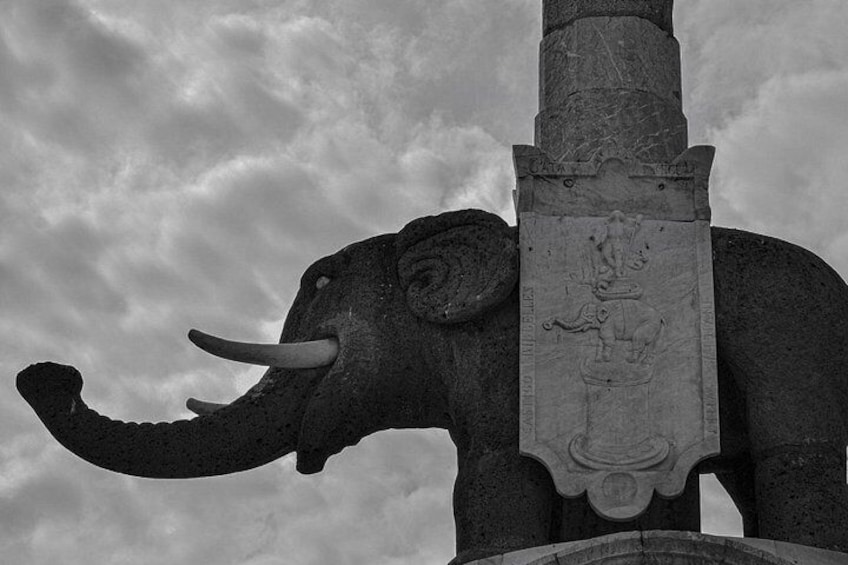 A stone elephant statue with tusks and a relief sculpture on its back. 3