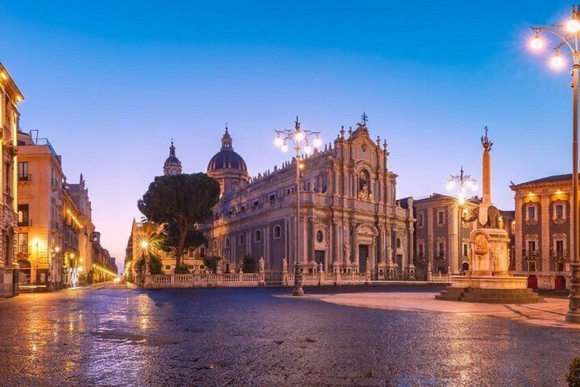 A historic square with a prominent church, a fountain, and surrounding buildings. 1