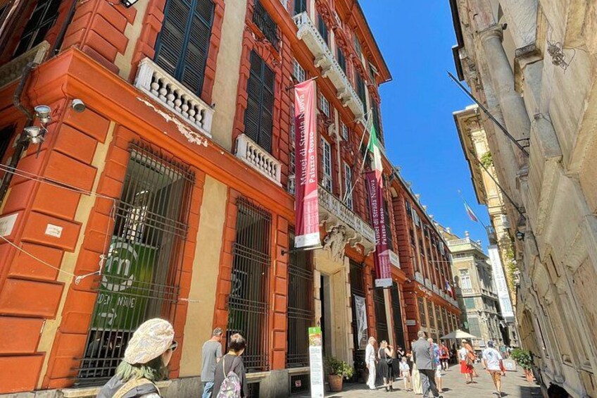 Una calle con edificios de color rojo y beige, gente caminando y un cielo azul despejado. 2