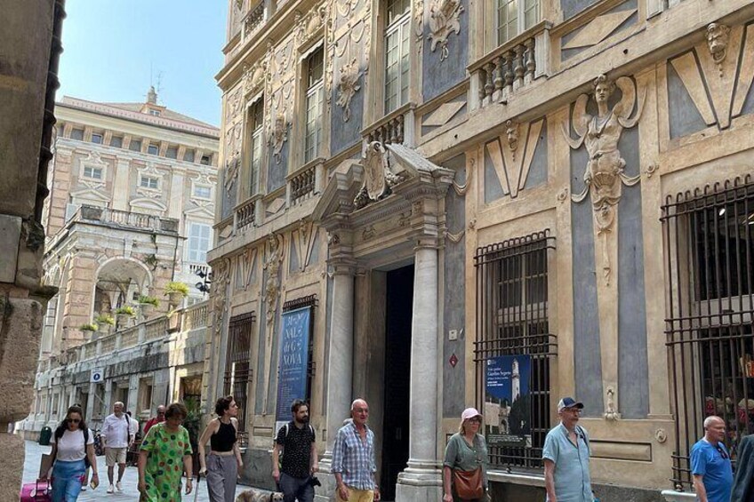 A historic building with ornate architecture, a group of people walking in front, and a clear blue sky. 3