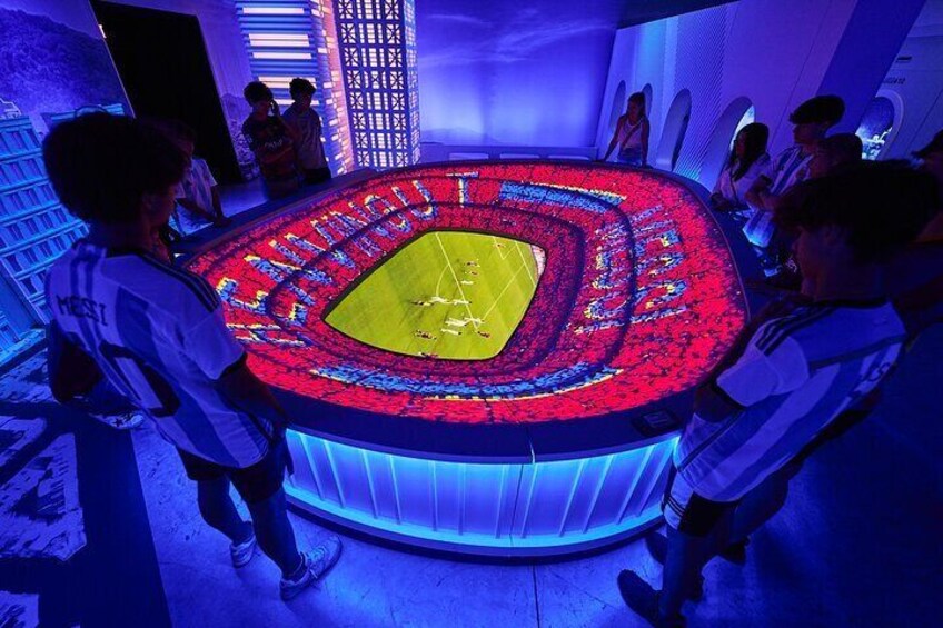 A large, illuminated stadium model surrounded by people. 3