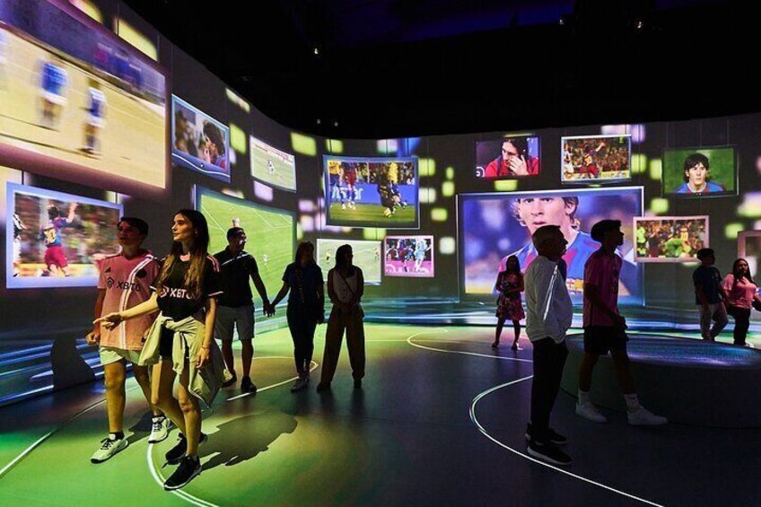 A group of people in a brightly lit indoor space with multiple screens displaying various images. 2