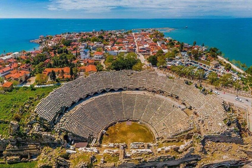 An ancient amphitheater surrounded by a coastal town with red-roofed buildings. 4
