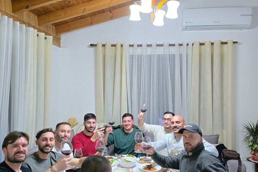 A group of people sitting around a table with food and drinks, in a room with curtains and a ceiling fan. 5