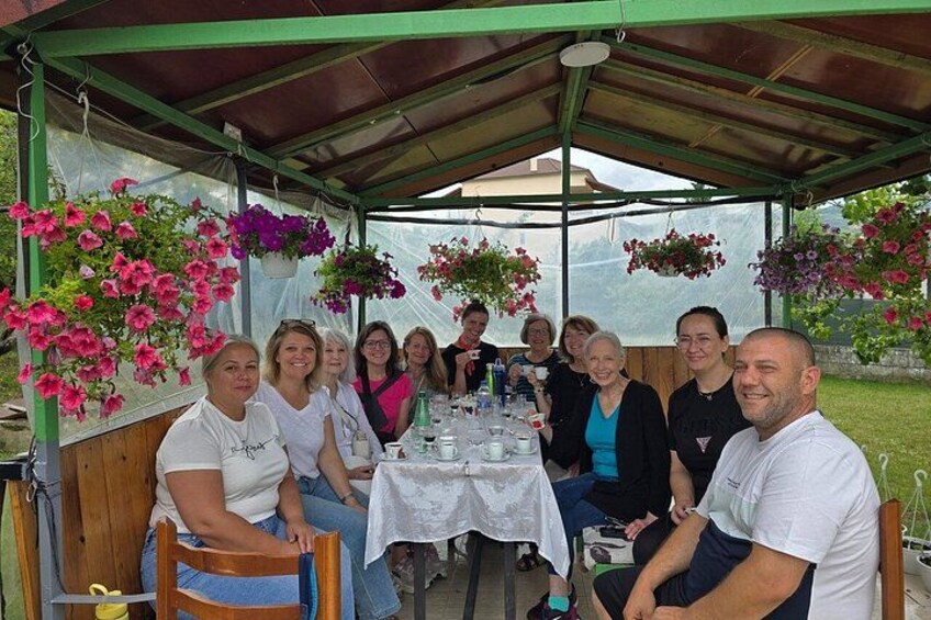 A group of people seated at a table under a covered area with hanging flower baskets. 3