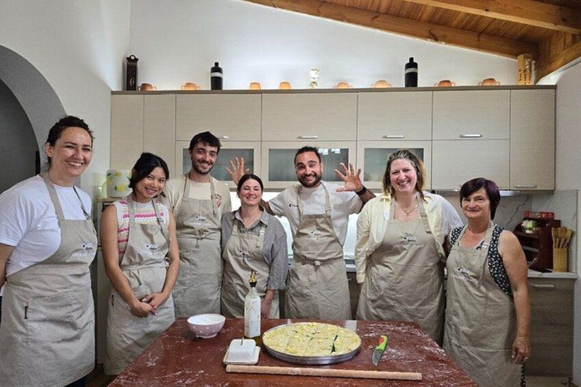 A group of people in aprons standing around a table with a large pie and baking tools. 4