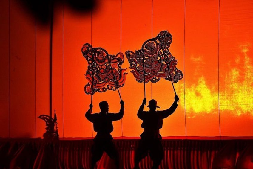 Two people holding up ornate, red and black patterned objects against a backdrop of a sunset. 1