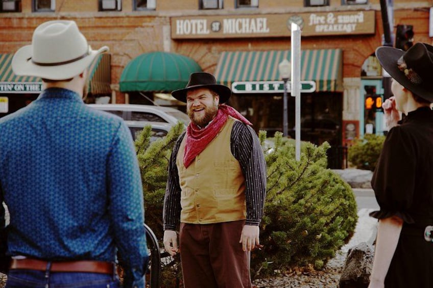 A man in a cowboy hat and vest standing on a street with a building labeled 'Hotel Michael' in the background. 3
