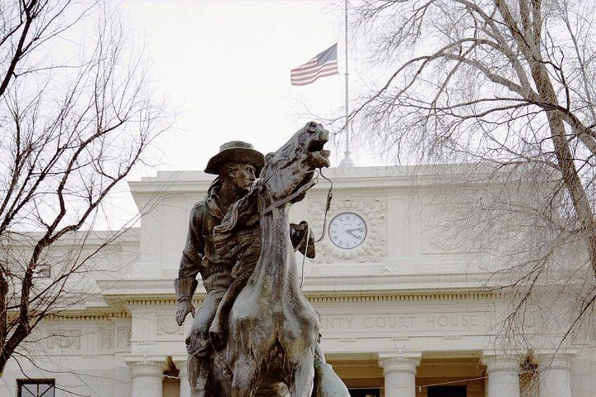 A statue of a man on a horse in front of a building with a clock and an American flag. 4