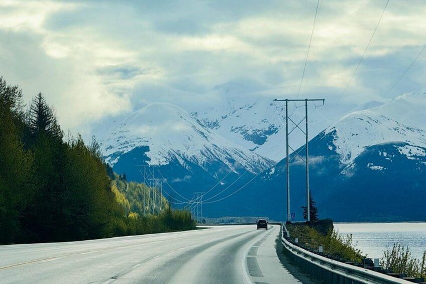 A road with a car, surrounded by mountains and a body of water. 1