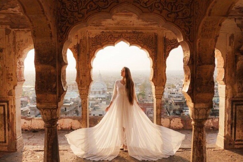 A person in a white dress standing in an ornate architectural structure with arches, overlooking a cityscape. 1