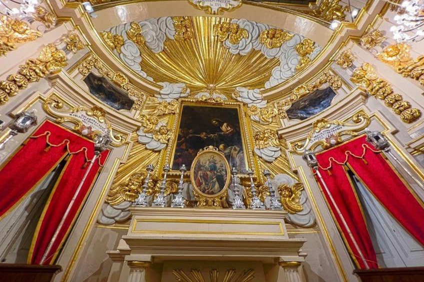 An ornate interior with gold accents, red drapes, and a central framed artwork. 4