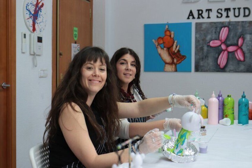 Two people engaged in a craft activity at a table with art supplies and a wall with art-themed decorations. 3