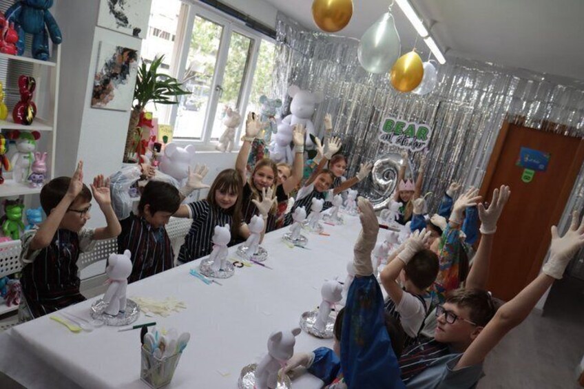 A group of children at a table with a white tablecloth, balloons, and a silver balloon arch. 5