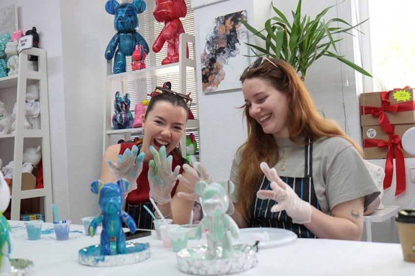 Two people painting ceramic figurines at a table with various tools and materials. 5
