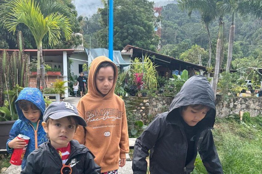 Four children outdoors, one in a blue jacket, one in an orange hoodie, and two in black jackets. 4