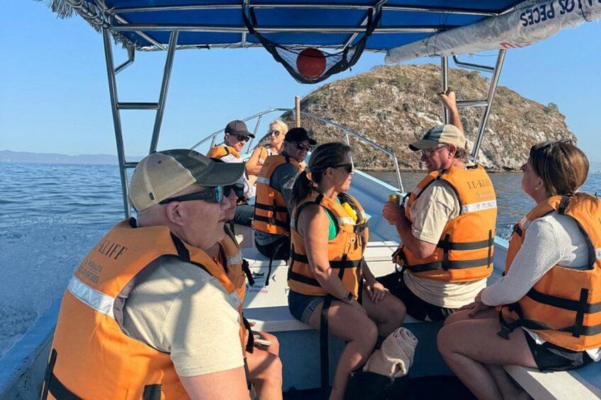 A group of people on a boat wearing life jackets, with a rocky island in the background. 5