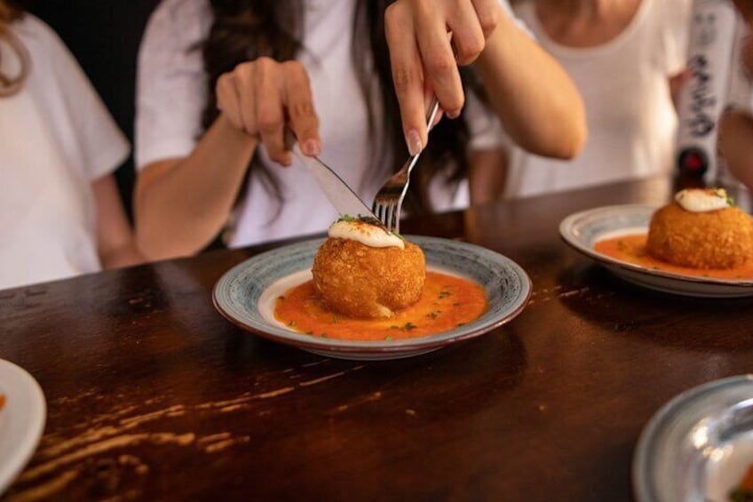 En person skærer en paneret ret med sauce på en tallerken. 1