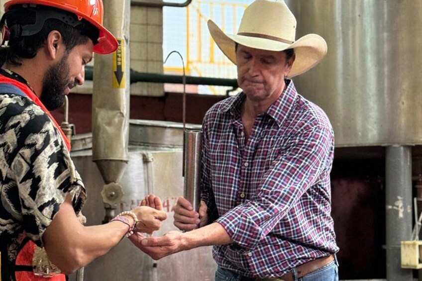 Two people exchanging something in an industrial setting with metal structures and a yellow sign. 5