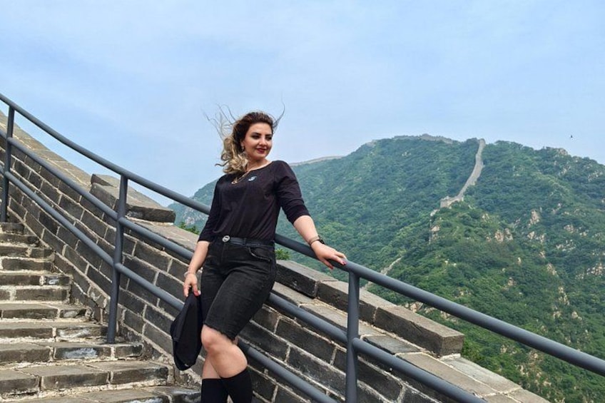 A person standing on a stone staircase with a railing, overlooking a mountainous landscape with a path. 5