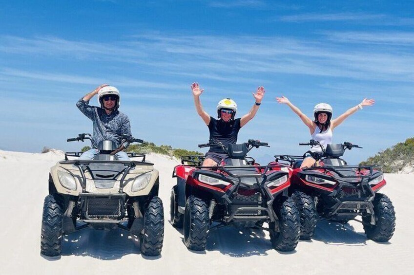 Tres personas en vehículos todo terreno sobre una playa arenosa, con cielos despejados. 3