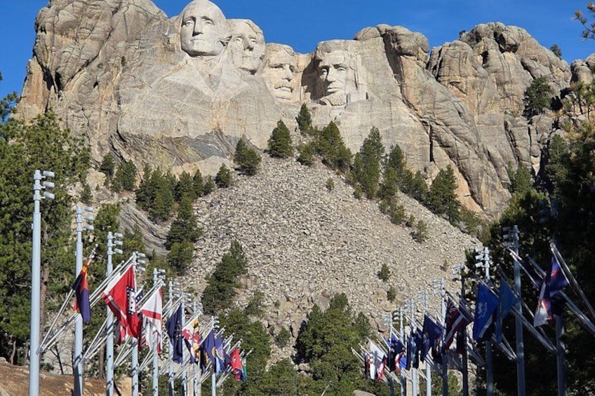 Mount Rushmore met vier presidentsgezichten, omgeven door bomen en vlaggen. 3
