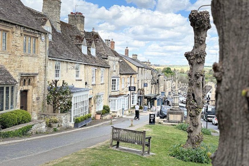 A quaint village street lined with stone buildings, a bench, and a tree. 4