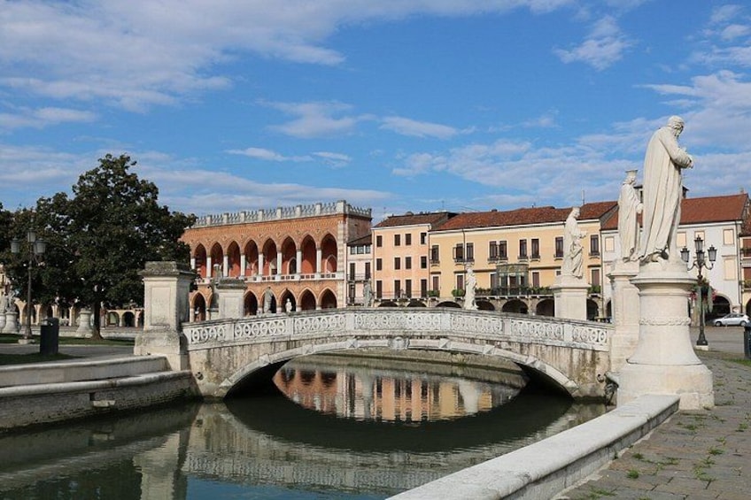 A stone bridge over a canal, with buildings and statues in the background. 2