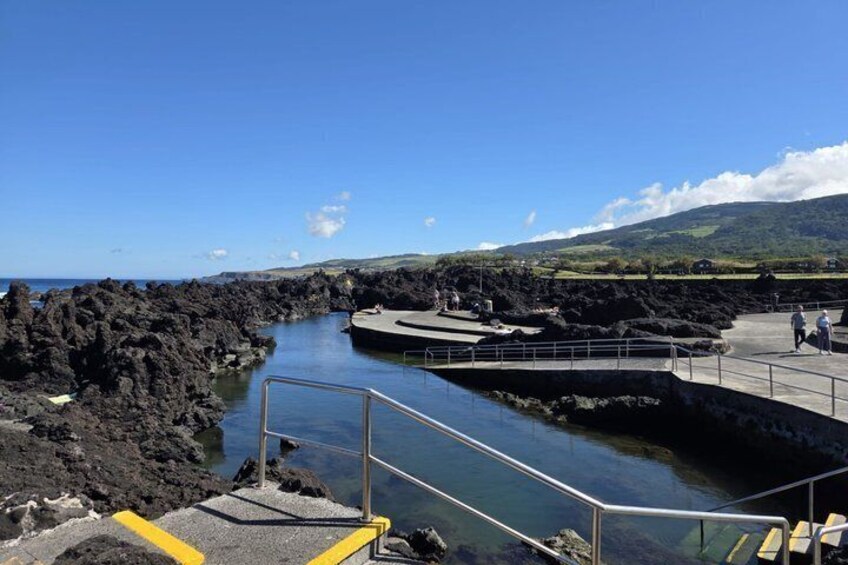Une zone côtière caractérisée par une côte rocheuse, un ciel bleu dégagé et une promenade pavée menant à un quai. 2