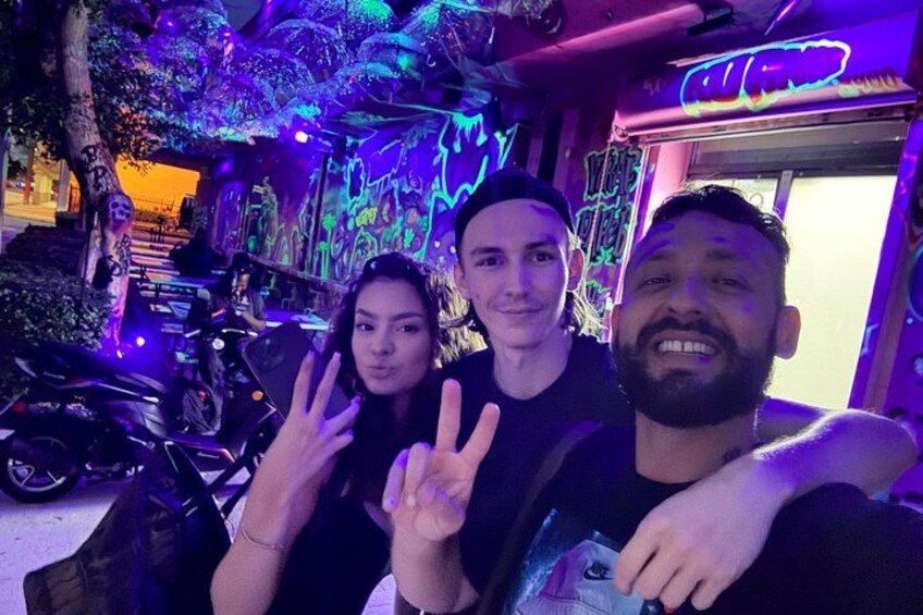 A group of people posing in a neon-lit urban setting with graffiti art. 4