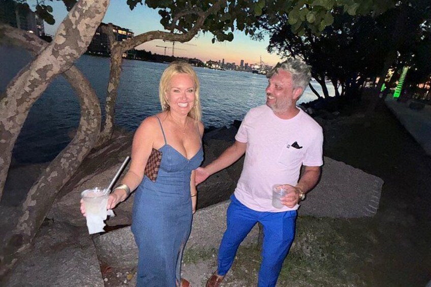 Two people standing by a waterfront with trees and a body of water in the background. 1