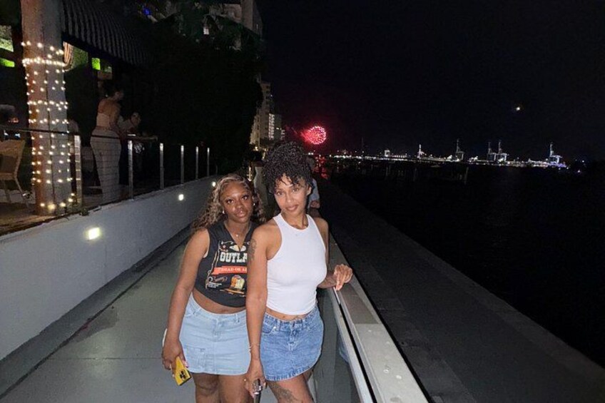Two people standing on a waterfront promenade at night. 2