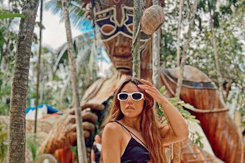 A person in a tropical setting with a large wooden structure and palm trees. 1