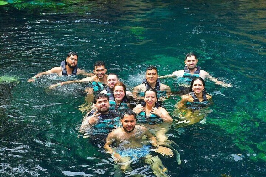 A group of people swimming in a clear body of water surrounded by greenery. 2