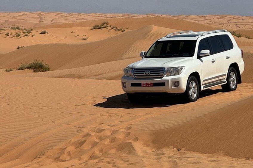 A white SUV on a sand dune in a desert landscape. 2