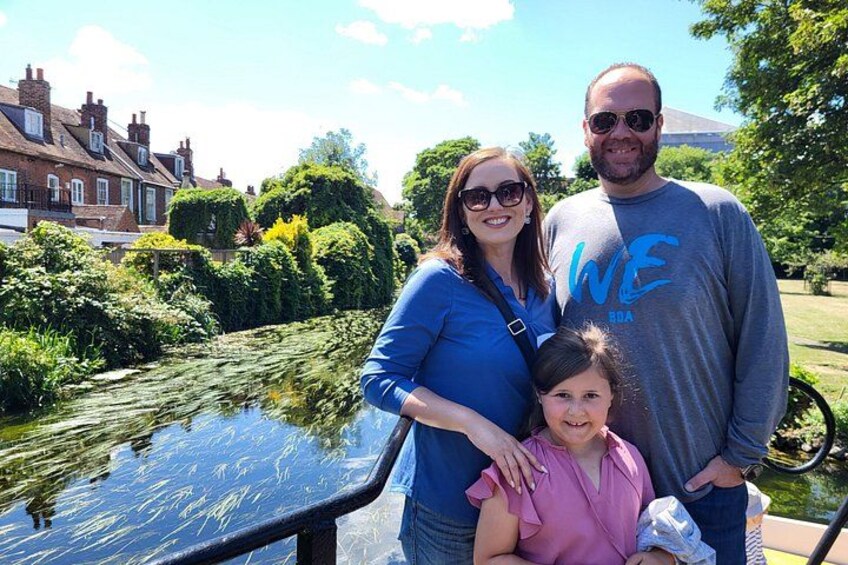 A family by a canal with houses in the background. 1