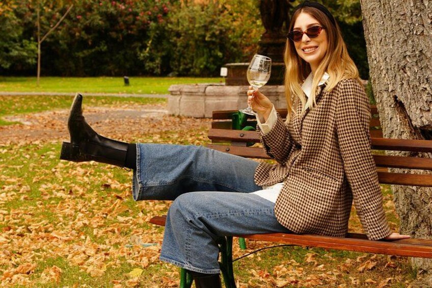 A person sitting on a bench in a park, holding a glass of wine. 1