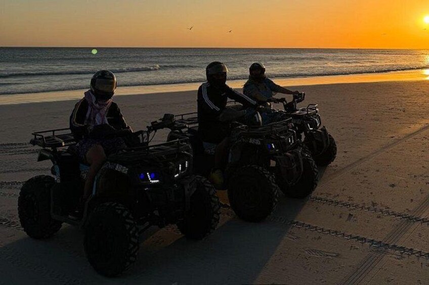 Two people on ATVs on a beach at sunset. 5