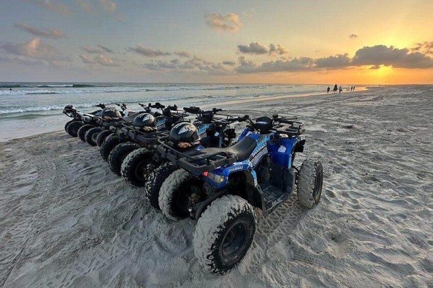 A row of ATVs parked on a sandy beach with the ocean in the background. 1