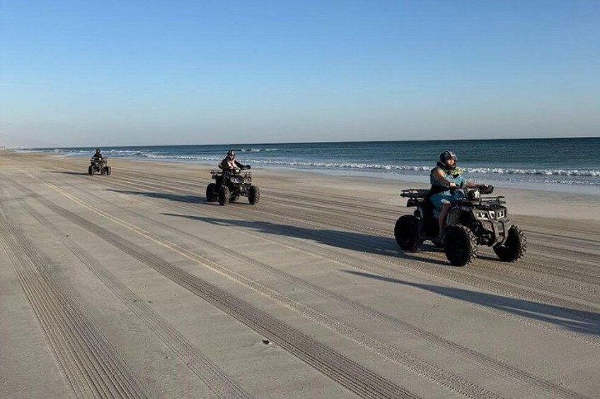 A beach with two people riding ATVs. 4