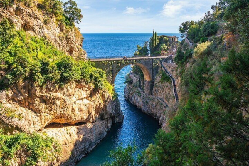 A stone bridge over a narrow water channel, surrounded by rocky cliffs and greenery. 2