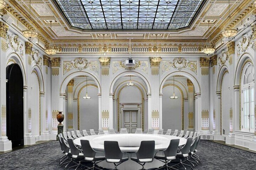 A grand conference room with a high ceiling, ornate gold detailing, and a central round table surrounded by chairs. 4
