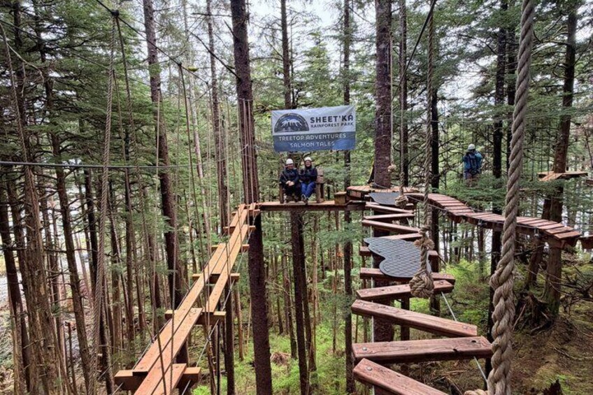 A forested area with wooden suspension bridges and a sign for Sheet'da Salmon Tales. 1