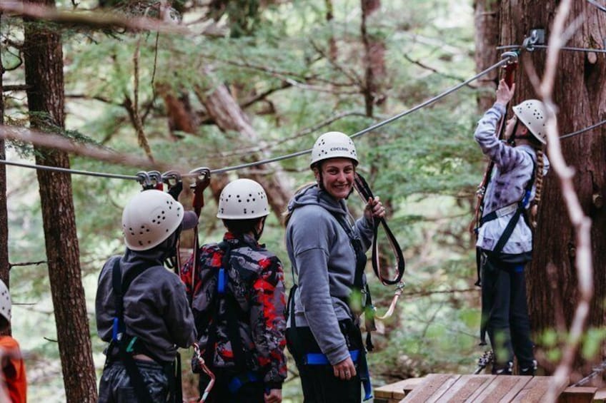 People wearing helmets and harnesses on a forested zipline course. 3