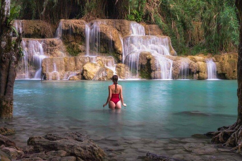 A woman in a red swimsuit standing in a clear pool of water with a waterfall in the background. 2